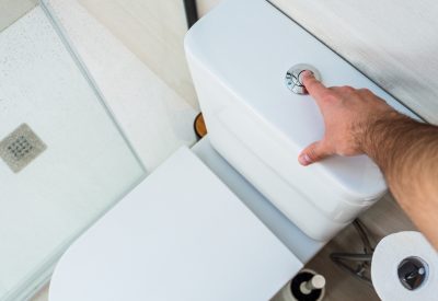 Man pressing the toilet flush button in a renovated white bathroom