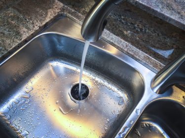 stainless steel kitchen sink with a garbage disposal and water running from the faucet