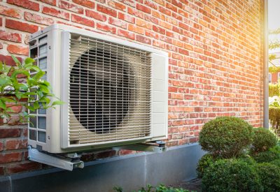 Angled shot of a wall-mounted air source heat pump against a brick wall